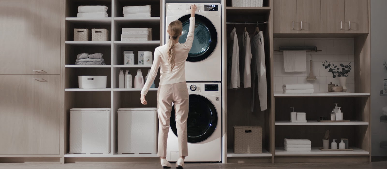 Femme ajustant machine à laver et sèche-linge LG dans une buanderie moderne avec étagères et penderie.